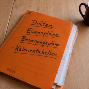 Orangefarbene Mappe voller Diätpläne auf einem Tisch – Symbol dafür, warum Diäten nicht funktionieren
